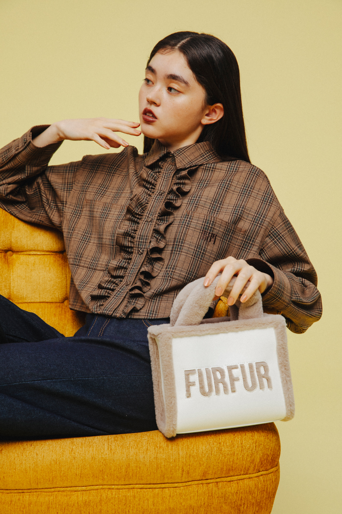 黄色いソファに座るフリルブラウスと FURFUR のバッグの着用カット